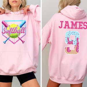 May include: Pink hooded sweatshirt with a softball graphic on the front and the name "JAMES" and the number "9" with a pink and blue ice cream design on the back.