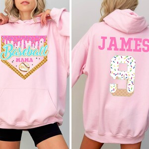 K&ouml;nnte beinhalten: Rosaer Hoodie mit Baseball-Motiv mit dem Text "Baseball Mama" auf der Vorderseite und ein rosaer Hoodie mit dem Text "JAMES" und der Nummer "9" auf der R&uuml;ckseite.