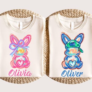 May include: Two white t-shirts with colorful bunny illustrations and names "Olivia" and "Oliver" printed on them.