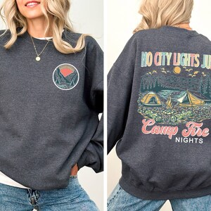 May include: A dark gray sweatshirt with a graphic print of a mountain scene and the text "NO CITY LIGHTS JUST CAMP FIRE NIGHTS". The front of the sweatshirt has a smaller graphic of a mountain scene.