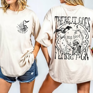 K&ouml;nnte beinhalten: Ein beiges T-Shirt mit einem schwarzen grafischen Aufdruck auf Vorder- und R&uuml;ckseite. Der vordere Aufdruck lautet "There it goes" und der hintere Aufdruck lautet "There it goes my last flying f*ck".