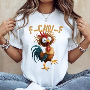 May include: White t-shirt featuring a cartoon rooster with wide eyes and an open beak. The rooster has a red comb, brown feathers, and a blue tail. The text "F-CAW-F" is printed above the rooster in a gold color.