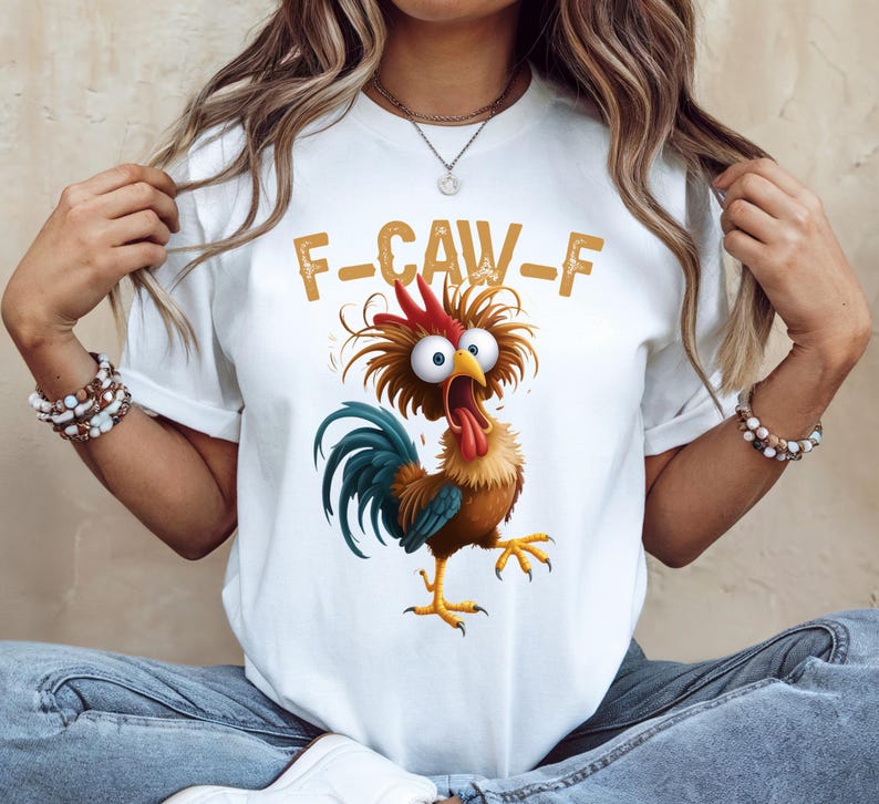 May include: White t-shirt featuring a cartoon rooster with wide eyes and an open beak. The rooster has a red comb, brown feathers, and a blue tail. The text "F-CAW-F" is printed above the rooster in a gold color.