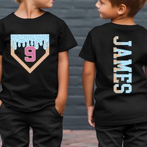 May include: Two black t-shirts with a blue and white ice cream design. One shirt has the number "9" in a pink baseball diamond. The other shirt has the name "JAMES" in a vertical design.