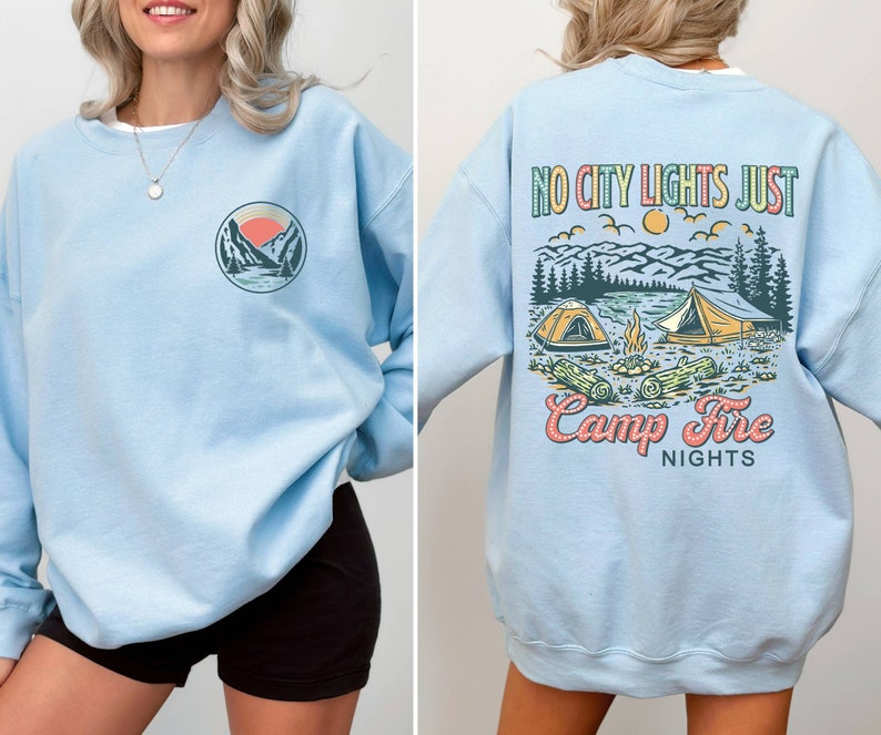 May include: Light blue sweatshirt with a graphic print of a sunset over mountains and the text "No City Lights Just Camp Fire Nights" on the back. The front of the sweatshirt has a smaller graphic of the sunset over mountains.