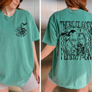 K&ouml;nnte beinhalten: Ein gr&uuml;nes T-Shirt mit einem Skelett-Motiv und dem Text "There it goes my last flying f*ck".