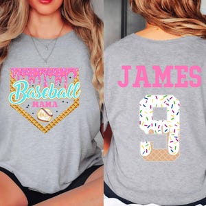 May include: Gray t-shirt with a pink baseball diamond graphic that says "Baseball Mama" and a waffle cone with sprinkles. The back of the shirt has the name "JAMES" in pink letters and a waffle cone with sprinkles in the shape of the number 9.