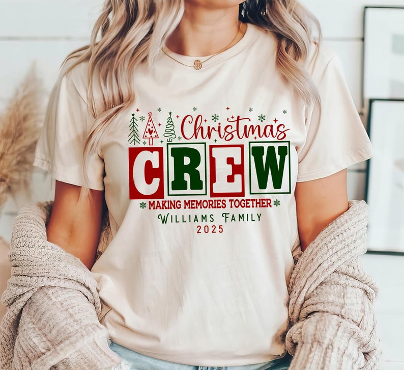 May include: A cream-coloured t-shirt with the words "Christmas Crew" in red and green, along with the text "Making Memories Together" and "Williams Family 2025". The shirt features Christmas tree graphics.