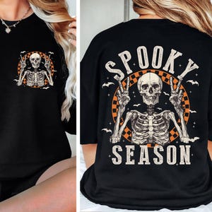 Puede incluir: Camiseta negra con un gr&aacute;fico de esqueleto y el texto "Spooky Season" en la espalda. El esqueleto est&aacute; sosteniendo dos signos de paz y est&aacute; rodeado de murci&eacute;lagos.