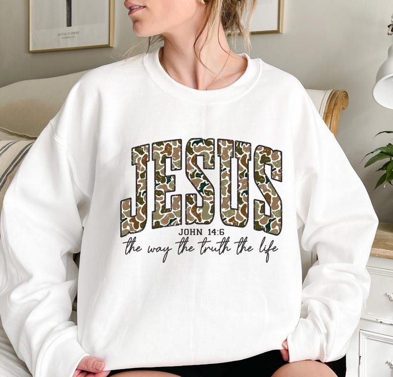 May include: White sweatshirt with the word "JESUS" in a camouflage pattern across the chest. Below the word "JESUS" is the text "JOHN 14:6" and "the way the truth the life" in black font.