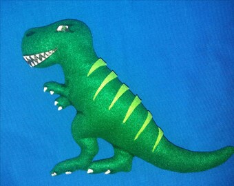 Może przedstawiać: Zielona zabawka dinozaura z filcu z wzorem jasnozielonych pasków. Dinozaur stoi na niebieskim tle.