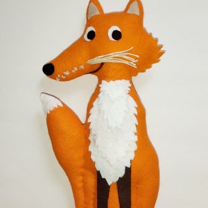 Könnte beinhalten: Ein orangefarbener Filz-Fuchs mit weißem Fell auf der Brust und einer schwarzen Nase. Der Fuchs hat braune Filzbeine und schwarze Augen.