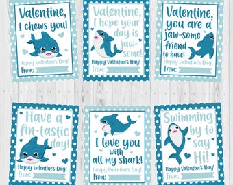 May include: Six blue and white Valentine's Day cards with shark illustrations and puns. The cards say "Valentine, I chews you!" "Valentine, I hope your day is jaw-some!" "Valentine, you are a jaw-some friend to have!" "Have a fin-tastic day!" "I love you with all my shark!" and "Swimming by to say Hi!"