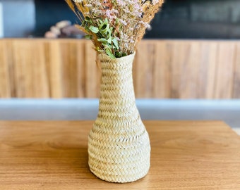 May include: A woven wicker vase with a narrow neck and a wide base, filled with a bouquet of dried flowers in shades of white, beige, and brown.