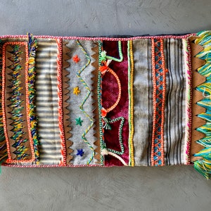 May include: A colourful, rectangular cushion with a variety of textures and patterns, including stripes, zigzags, and embroidery. The cushion has fringe on all four sides.
