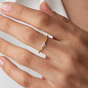 May include: A simple gold band ring with a small, clear gemstone in the centre.