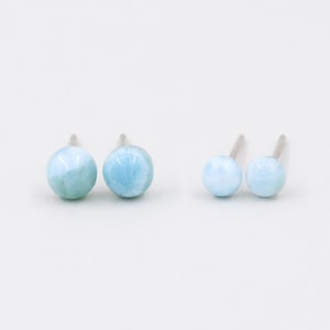 May include: A pair of blue gemstone stud earrings. The earrings are made of silver and have a round shape.