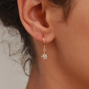May include: Gold hoop earrings with a dangling star charm featuring clear cubic zirconia stones.