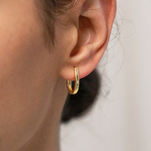 Könnte beinhalten: Nahaufnahme eines Ohrs mit einem kleinen, goldenen Creolenohrring. Der Ohrring ist schlicht und elegant und wäre eine großartige Ergänzung für jede Schmucksammlung.