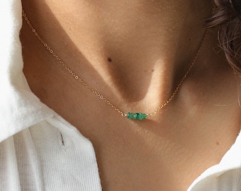 May include: A delicate gold chain necklace with a small cluster of emerald green gemstones.
