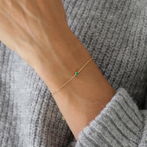 Pode incluir: Um delicado bracelete de corrente dourada com uma única pequena gema verde.