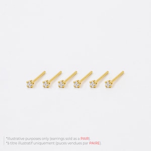 May include: Six gold-colored stud earrings with a small, clear, square-cut gemstone at the end of each post. The earrings are arranged in a row against a white background. Text at the bottom states, "illustrative purposes only (earrings sold as a PAIR)."