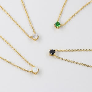 May include: Four gold necklaces with different colored gemstones. The necklaces feature a small, round, white, black, green, and opal gemstone.