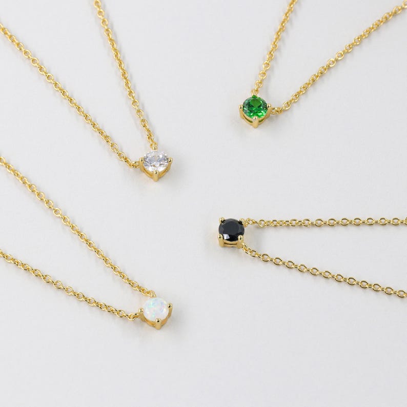 May include: Four gold necklaces with different colored gemstones. The necklaces feature a small, round, white, black, green, and opal gemstone.