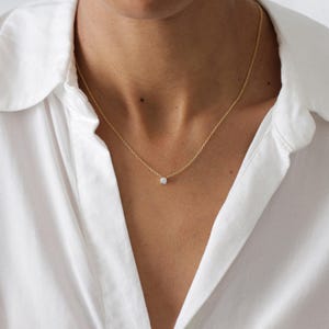 May include: A delicate gold chain necklace with a small, clear gemstone pendant.
