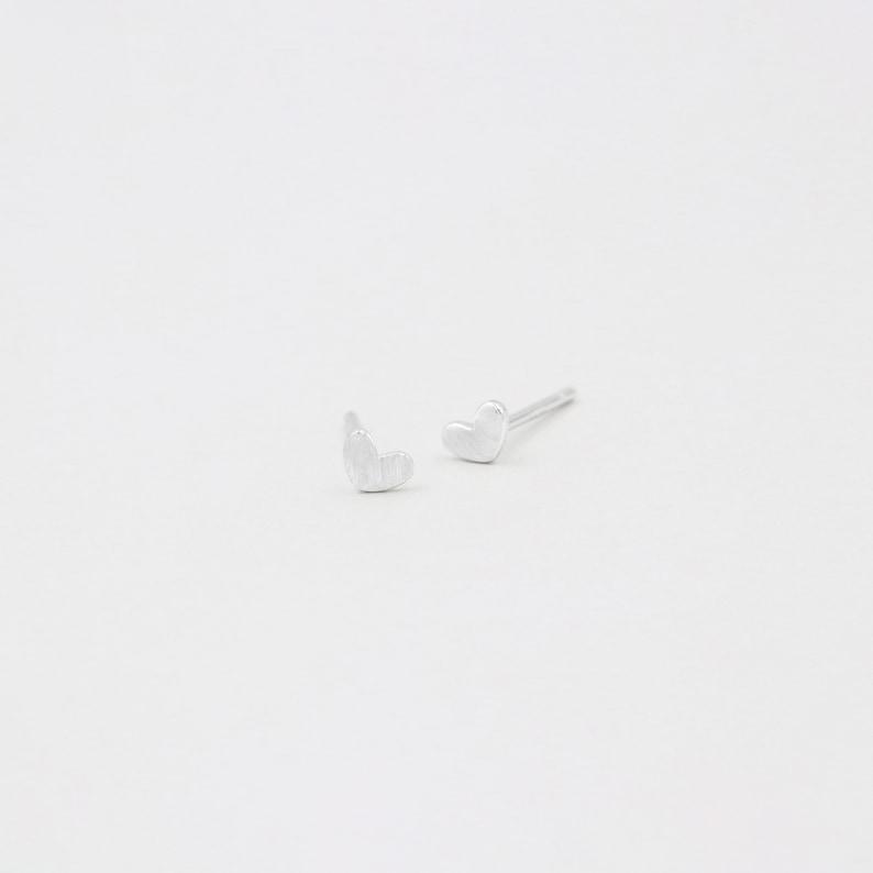 May include: A pair of silver heart-shaped stud earrings.