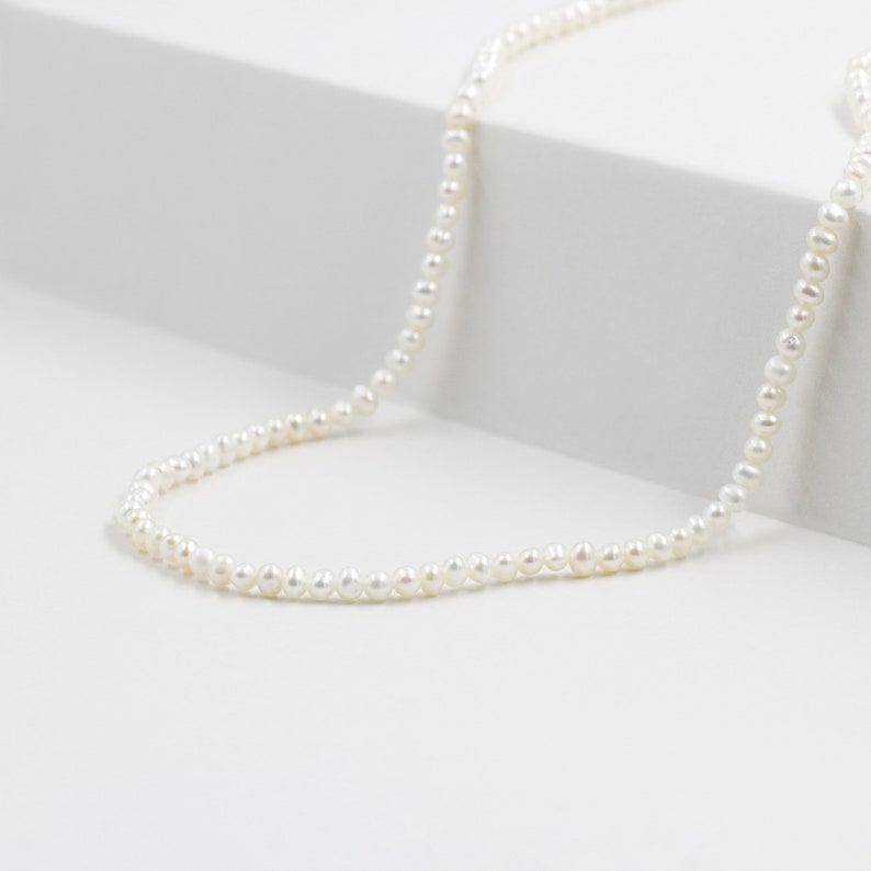Puede incluir: Un collar de perlas blancas sencillo con peque&ntilde;as perlas espaciadas uniformemente.