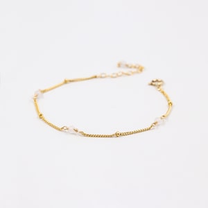Puede incluir: Un delicado brazalete de cadena dorada con peque&ntilde;as cuentas blancas. El brazalete tiene un dise&ntilde;o sencillo y es perfecto para el uso diario.