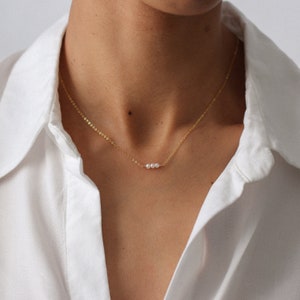 Puede incluir: Un delicado collar de cadena dorada con tres peque&ntilde;as perlas blancas en fila.