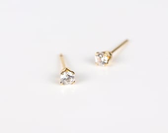 May include: A pair of gold stud earrings with small, clear round stones.
