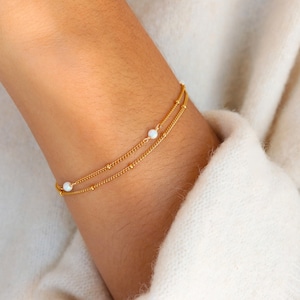 Peut inclure: Un bracelet délicat en chaîne dorée à deux rangs avec de petites perles d'opale blanche.
