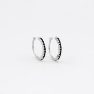 May include: A pair of silver ear cuffs with a row of black cubic zirconia stones around the edge.