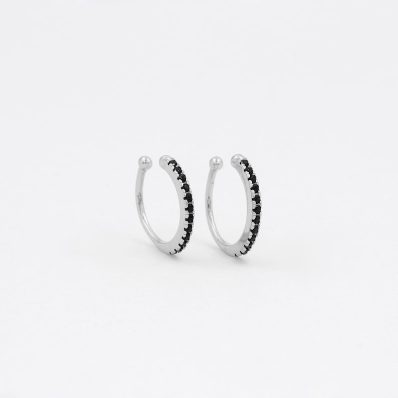 May include: A pair of silver ear cuffs with a row of black cubic zirconia stones around the edge.