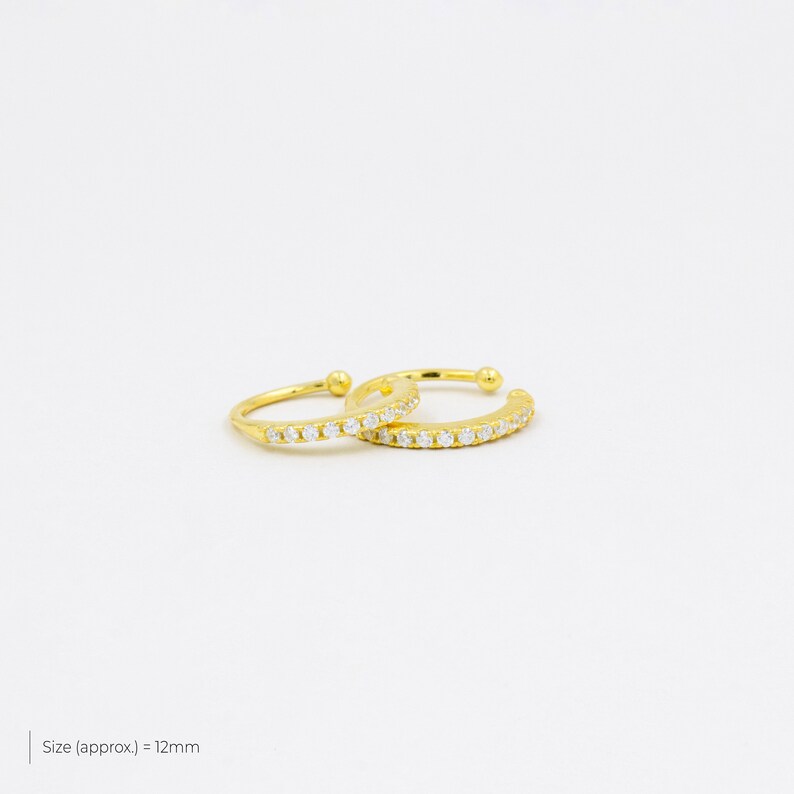 May include: Two gold ear cuffs with a row of clear cubic zirconia stones. Size (approx.) = 12mm.