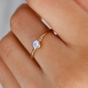 Peut inclure: Une bague en or avec une pierre de lune ronde et irisée.