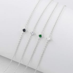 Pu&ograve; includere: Quattro braccialetti a catena d'argento con pietre preziose di diversi colori. I braccialetti presentano una pietra preziosa nera, bianca, verde e trasparente.