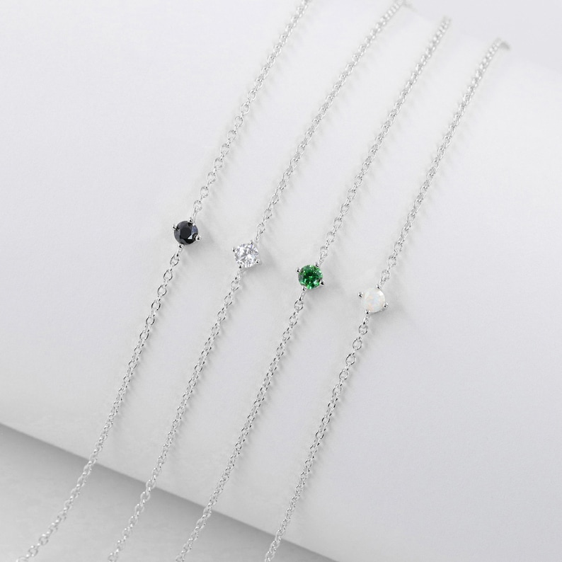 Pu&ograve; includere: Quattro braccialetti a catena d'argento con pietre preziose di diversi colori. I braccialetti presentano una pietra preziosa nera, bianca, verde e trasparente.
