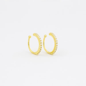 May include: A pair of gold ear cuffs with a row of clear cubic zirconia stones around the edge.
