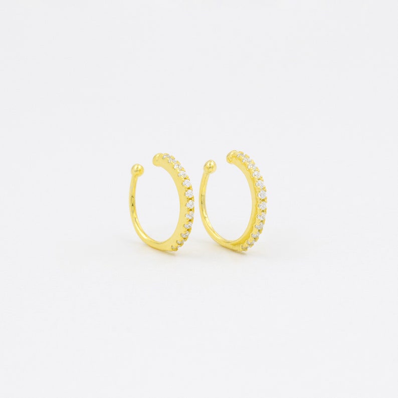 May include: A pair of gold ear cuffs with a row of clear cubic zirconia stones around the edge.