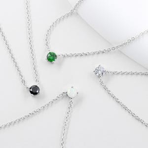 May include: Four silver necklaces with different colored gemstones. The necklaces feature a single round gemstone pendant in black, white, green, and opal.