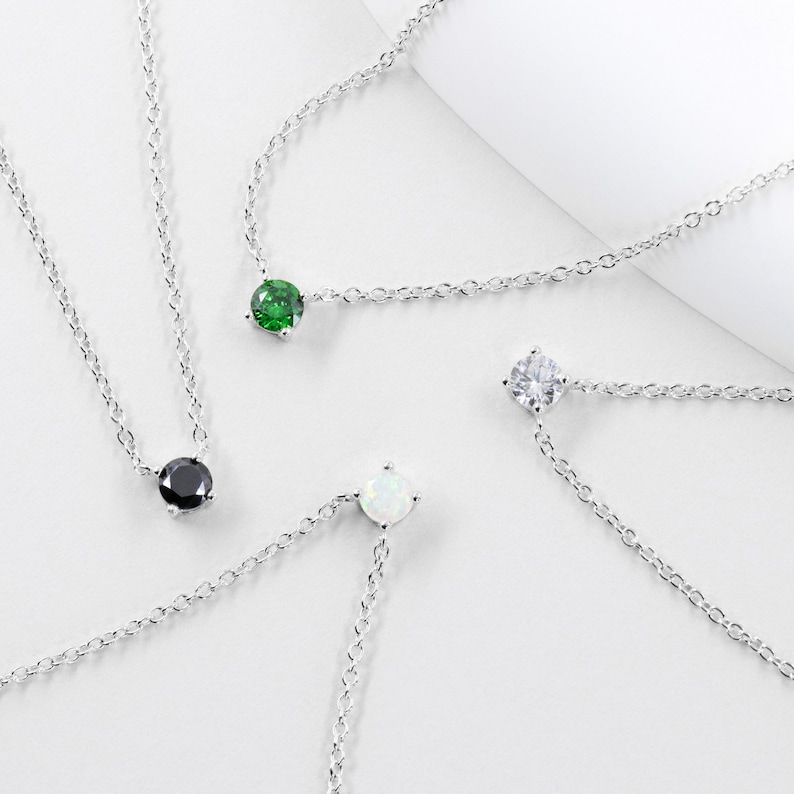 May include: Four silver necklaces with different colored gemstones. The necklaces feature a single round gemstone pendant in black, white, green, and opal.