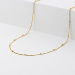 May include: A delicate gold chain necklace with small round beads spaced evenly along the chain.