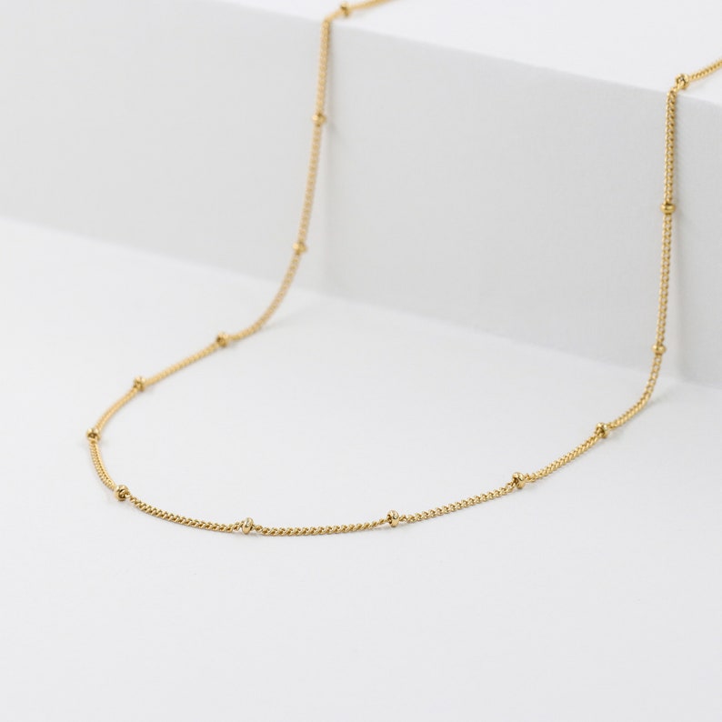 May include: A delicate gold chain necklace with small round beads spaced evenly along the chain.
