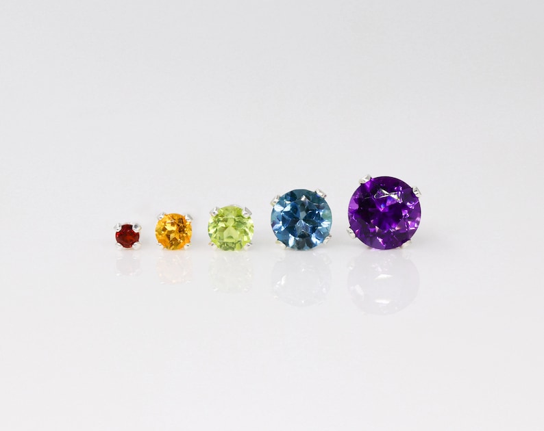 May include: Five round gemstones of different colors and sizes, set in silver. The gemstones are red, yellow, green, blue, and purple.