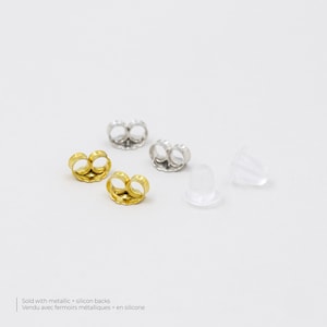 May include: Four earring backs, two gold and two silver, and two clear silicone earring backs. Sold with metallic + silicon backs. Vendu avec fermoirs metalliques + en silicone.