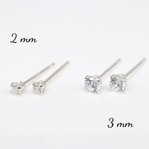 May include: Two pairs of silver stud earrings with clear cubic zirconia stones. The top pair has 2 mm stones and the bottom pair has 3 mm stones.